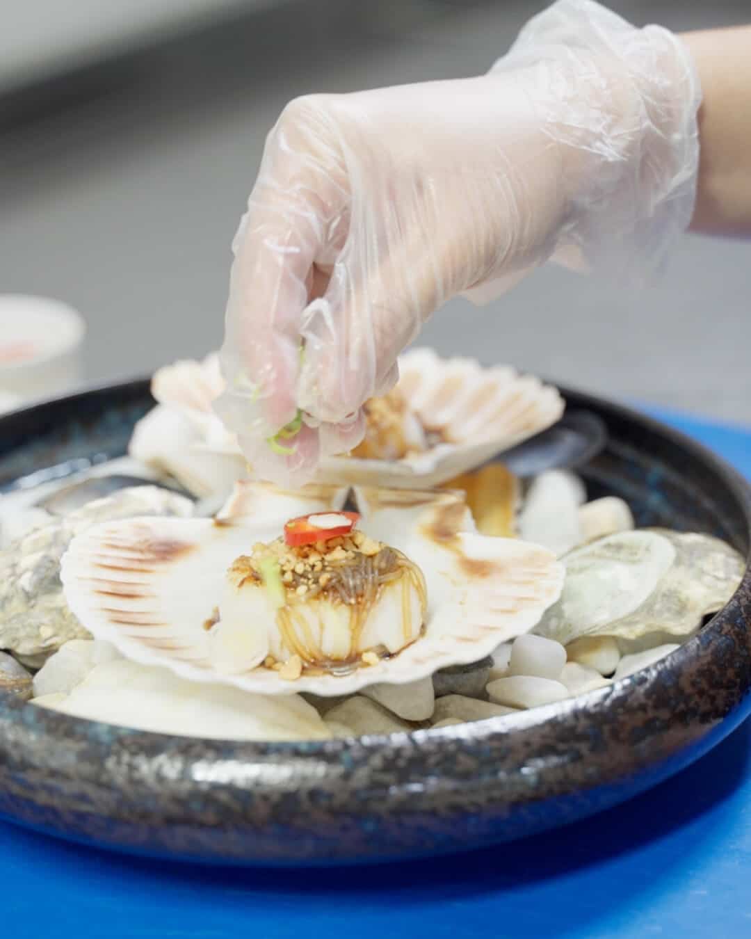 Chef-kok richt gegrilde coquilles aan op een bord met schelpen